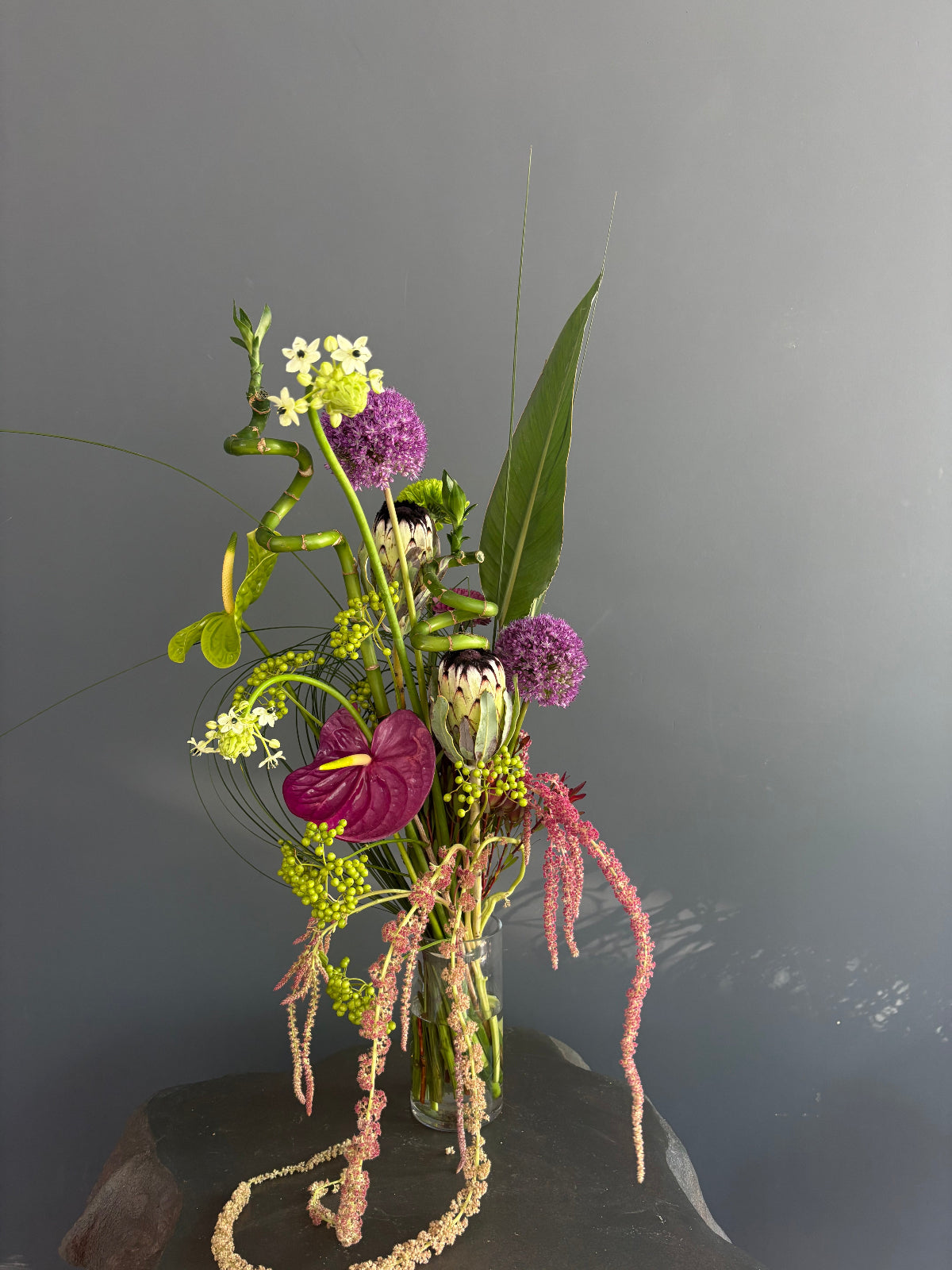 The Wild designer bouquet with burgundy anthurium, purple allium, hanging amaranthus, lucky bamboo, and green berries